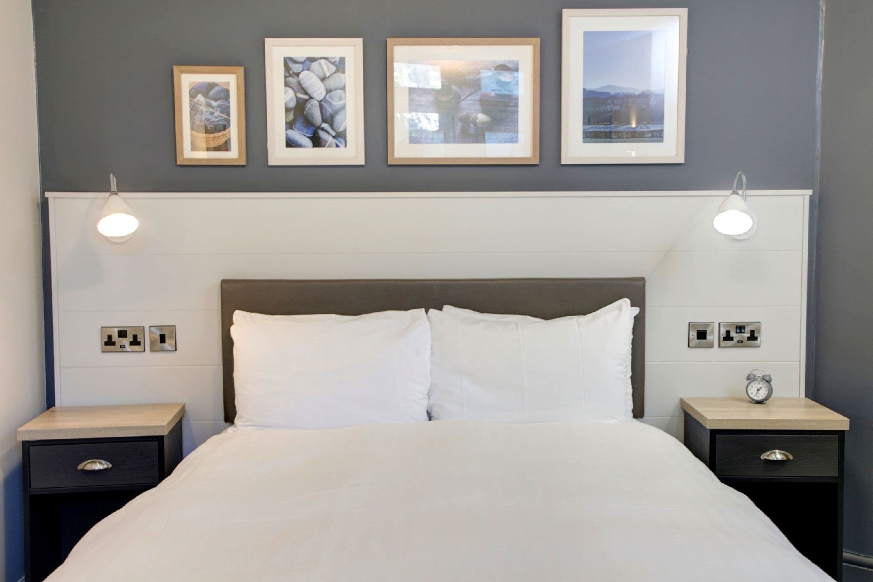 Une chambre d’hôtel bien rangée, avec un grand lit, deux tables de chevet et trois tableaux encadrés accrochés au mur.