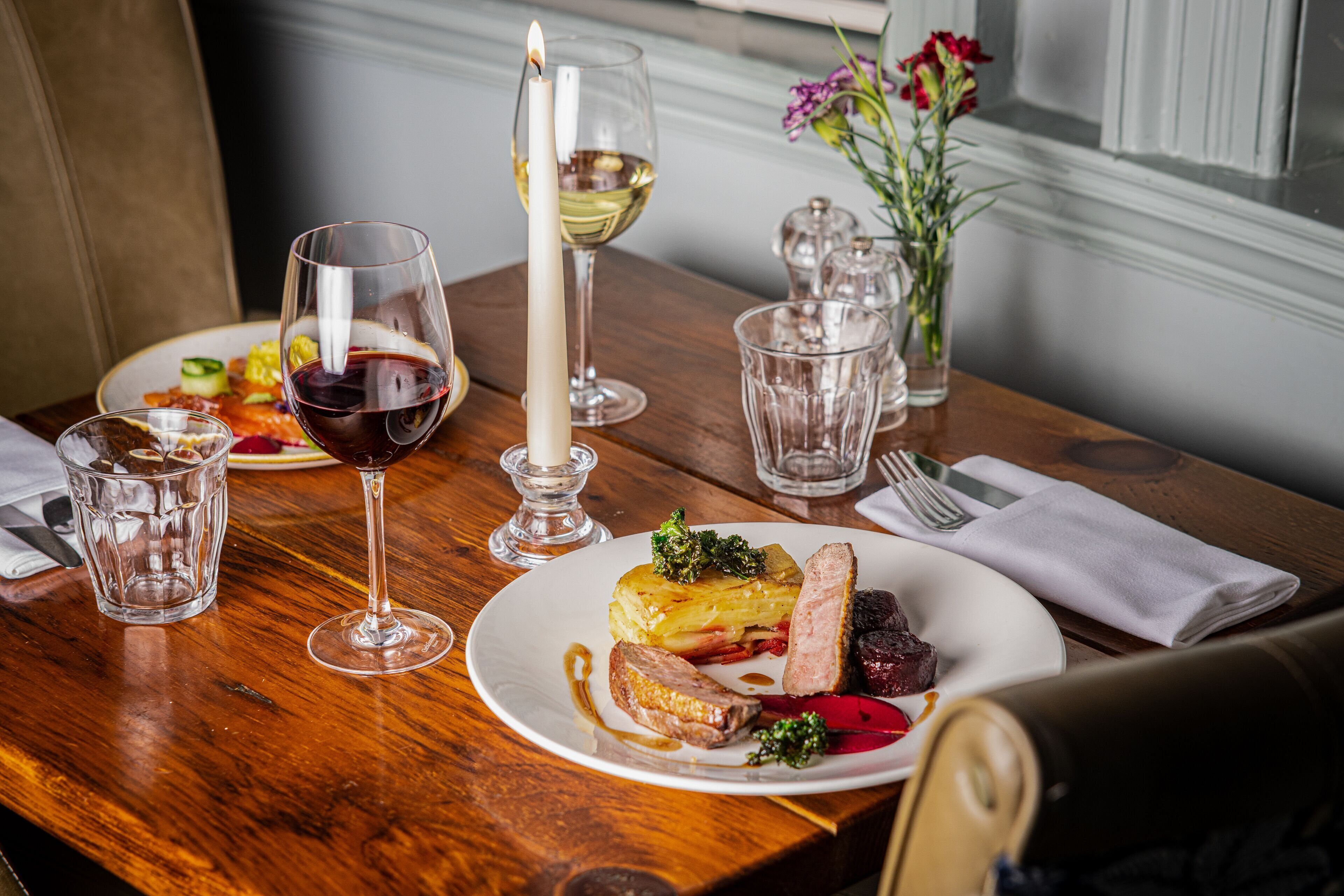 A dining table with plates of food, wine glasses, and a candle.