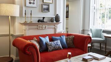 A living room with a red sofa, a coffee table with books and a glass of beer, a fireplace with decorative items, and framed pictures on the wall.