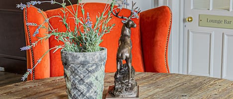 A wooden table with a potted plant and a deer statue. A red chair is behind the table. A door with a sign reading "Lounge Bar" is visible in the background.