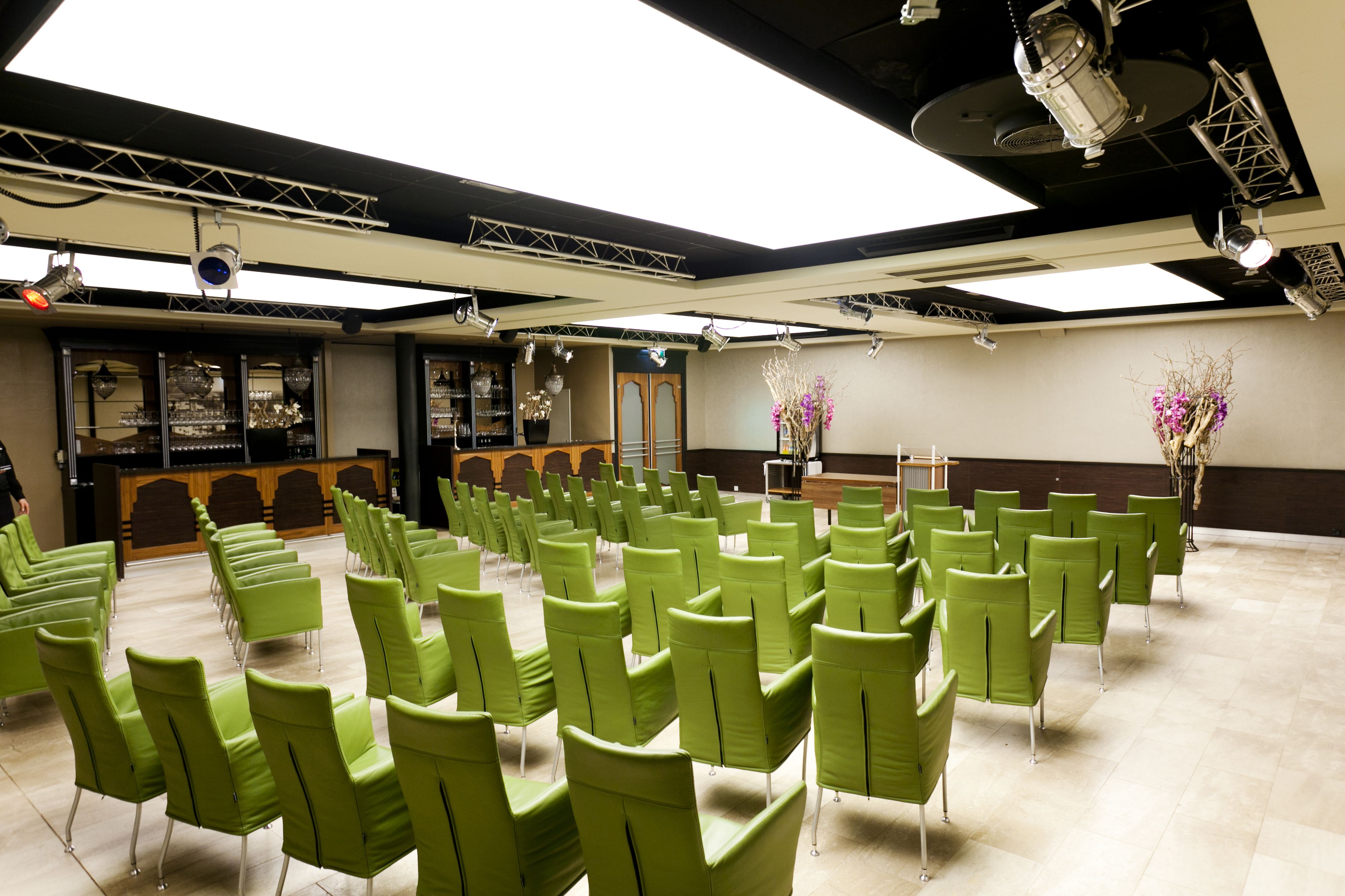 A conference room with rows of green chairs, a stage with a podium, and a reception area with a counter and glass display cases.