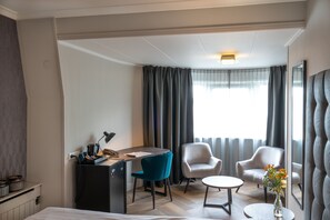 A hotel room with a bed, a desk with a lamp, two chairs, a small table with a vase, and a large window with curtains. - Fletcher Hotel-Restaurant De Korenbeurs (Made)