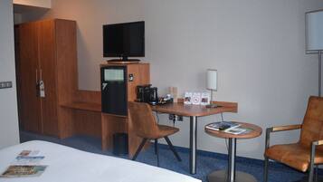 A hotel room with a bed, a desk with a computer, a television, and two chairs.