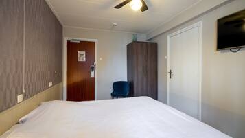 A hotel room with a large bed, a ceiling fan, a TV mounted on the wall, and a wooden door.