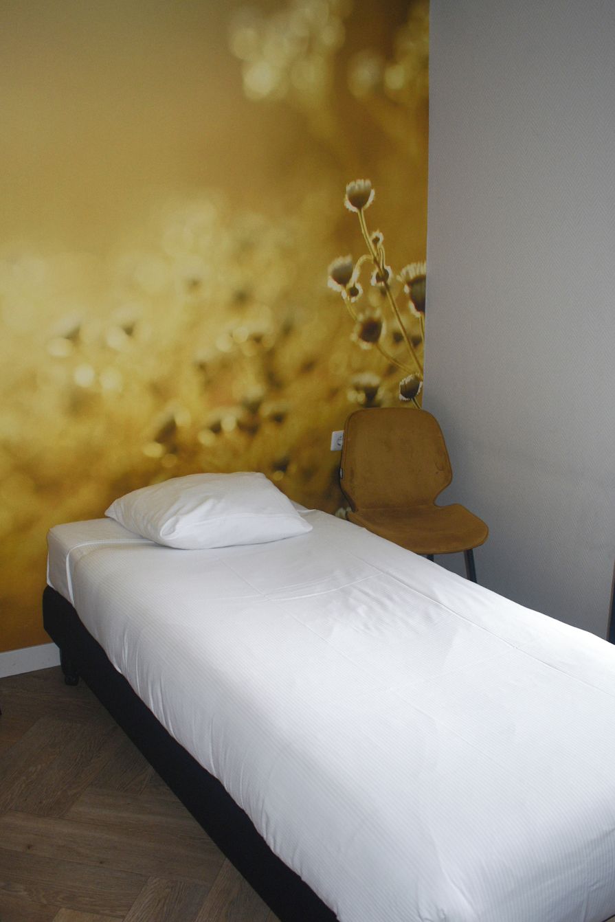 Una cama individual con ropa de cama blanca en una habitación con un gran mural en la pared de un paisaje dorado.