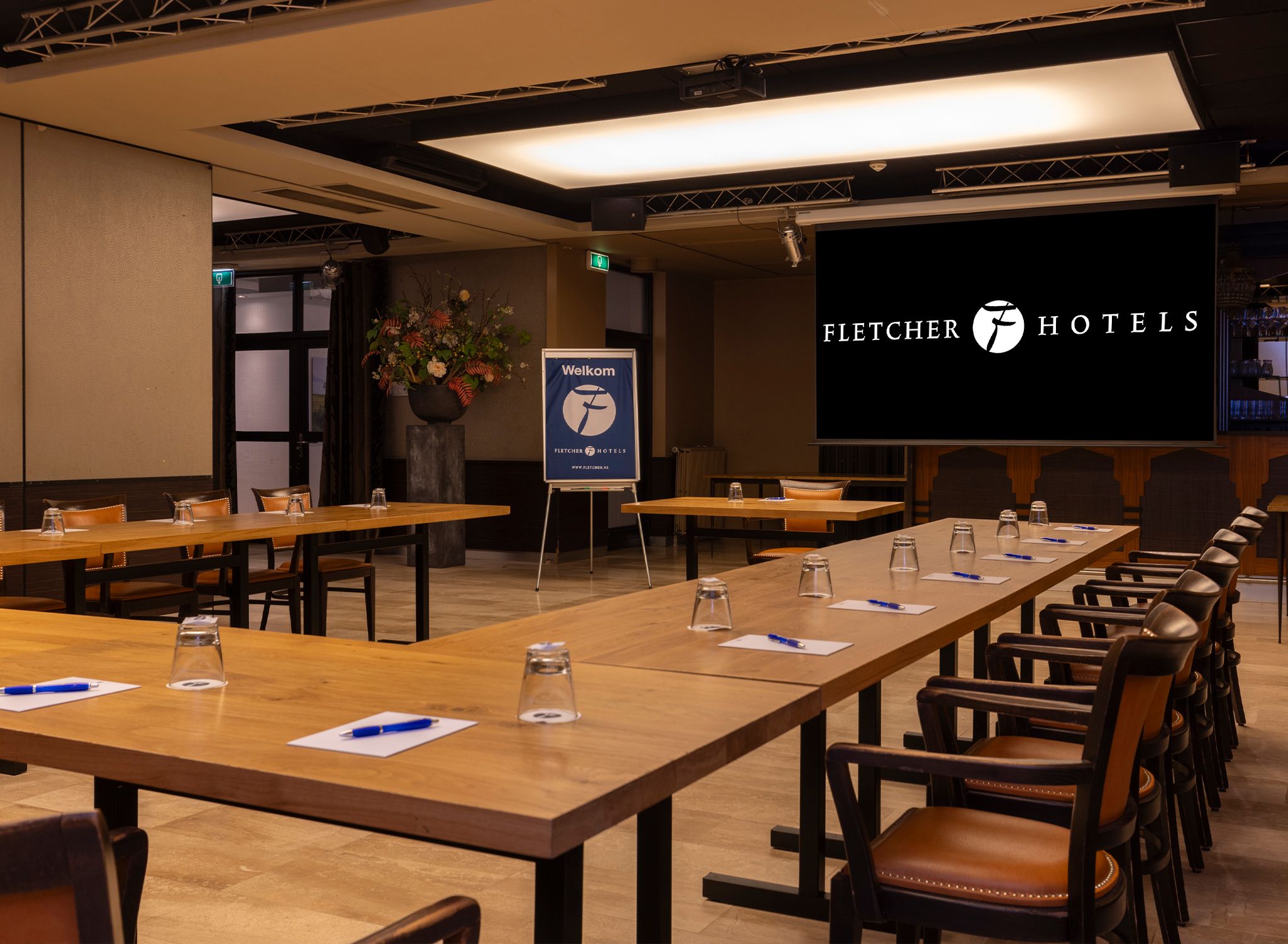 A conference room with long tables, chairs, and a large screen displaying 'Fletcher Hotels' branding.