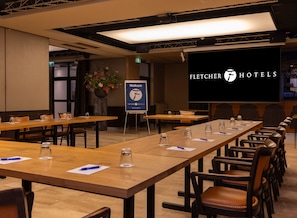 A conference room with long tables, chairs, and a large screen displaying 'Fletcher Hotels' branding. - Fletcher Hotel-Restaurant De Korenbeurs (Made)