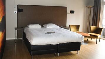 A modern hotel room with a large bed, a bedside table, a chair, and a floor lamp.
