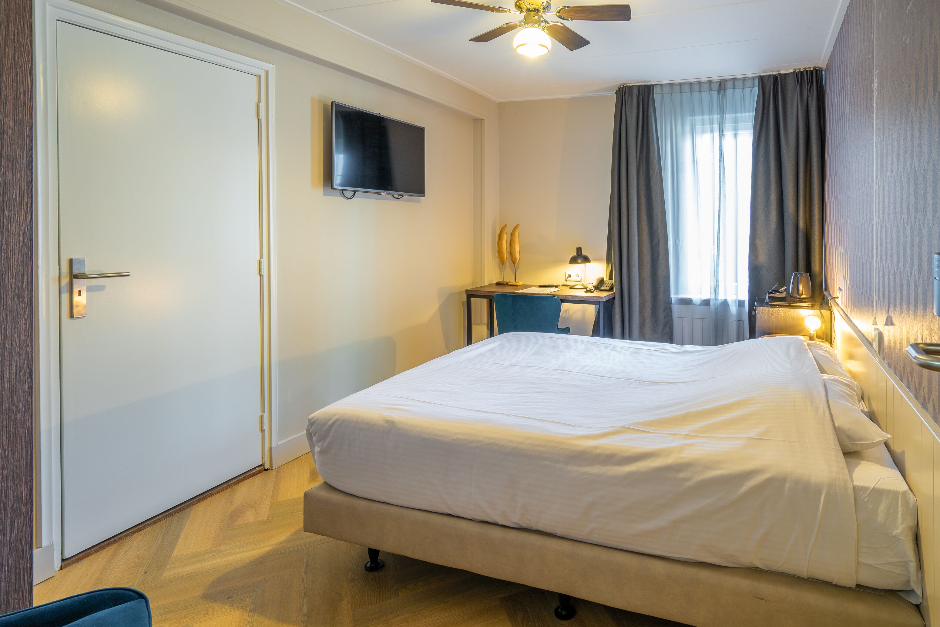 A hotel room with a bed, a desk, a television, and a ceiling fan.
