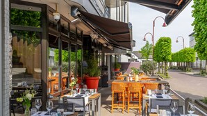 Un espace de restauration en plein air avec des tables prévues pour deux personnes, agrémenté d’un assortiment de chaises en bois et en osier.