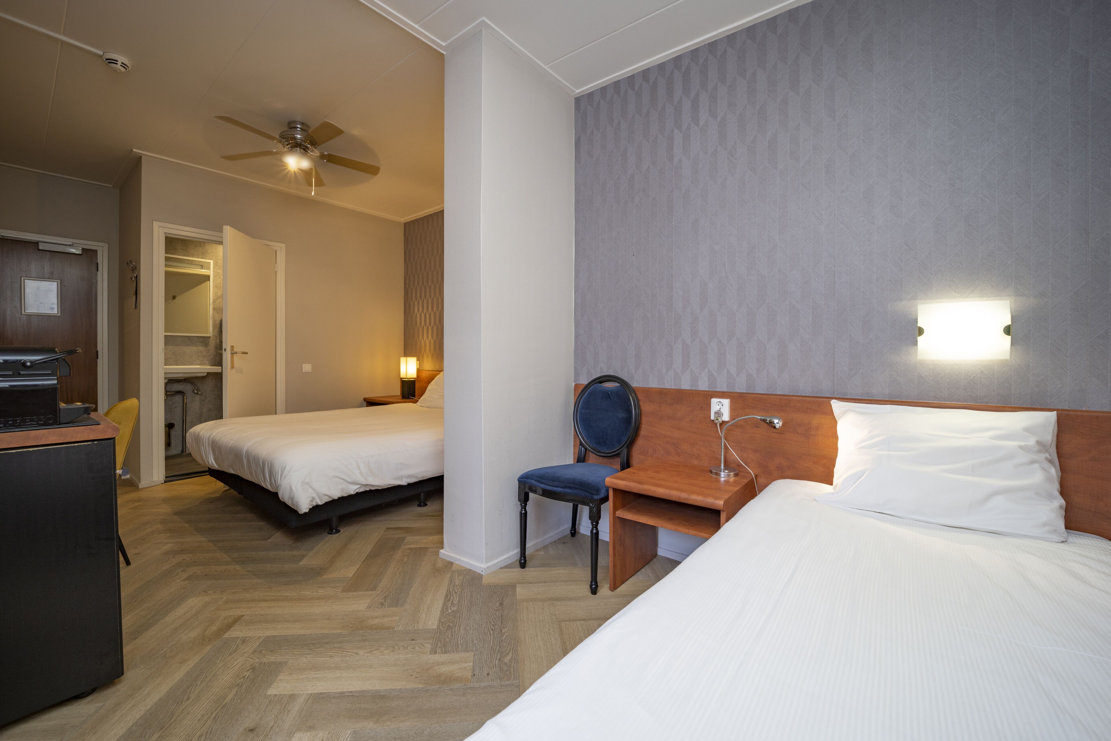 Een hotelkamer met twee bedden, een bureau, een stoel en een plafondventilator.