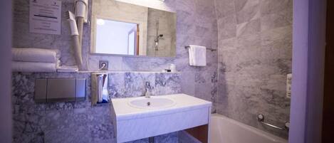 A bathroom with a marble wall, a sink, a mirror, a towel rack, a toilet, and a bathtub.