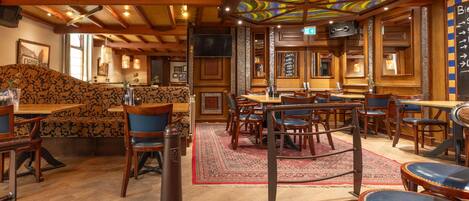 A restaurant interior with wooden beams, patterned seating, and a colorful stained glass ceiling.