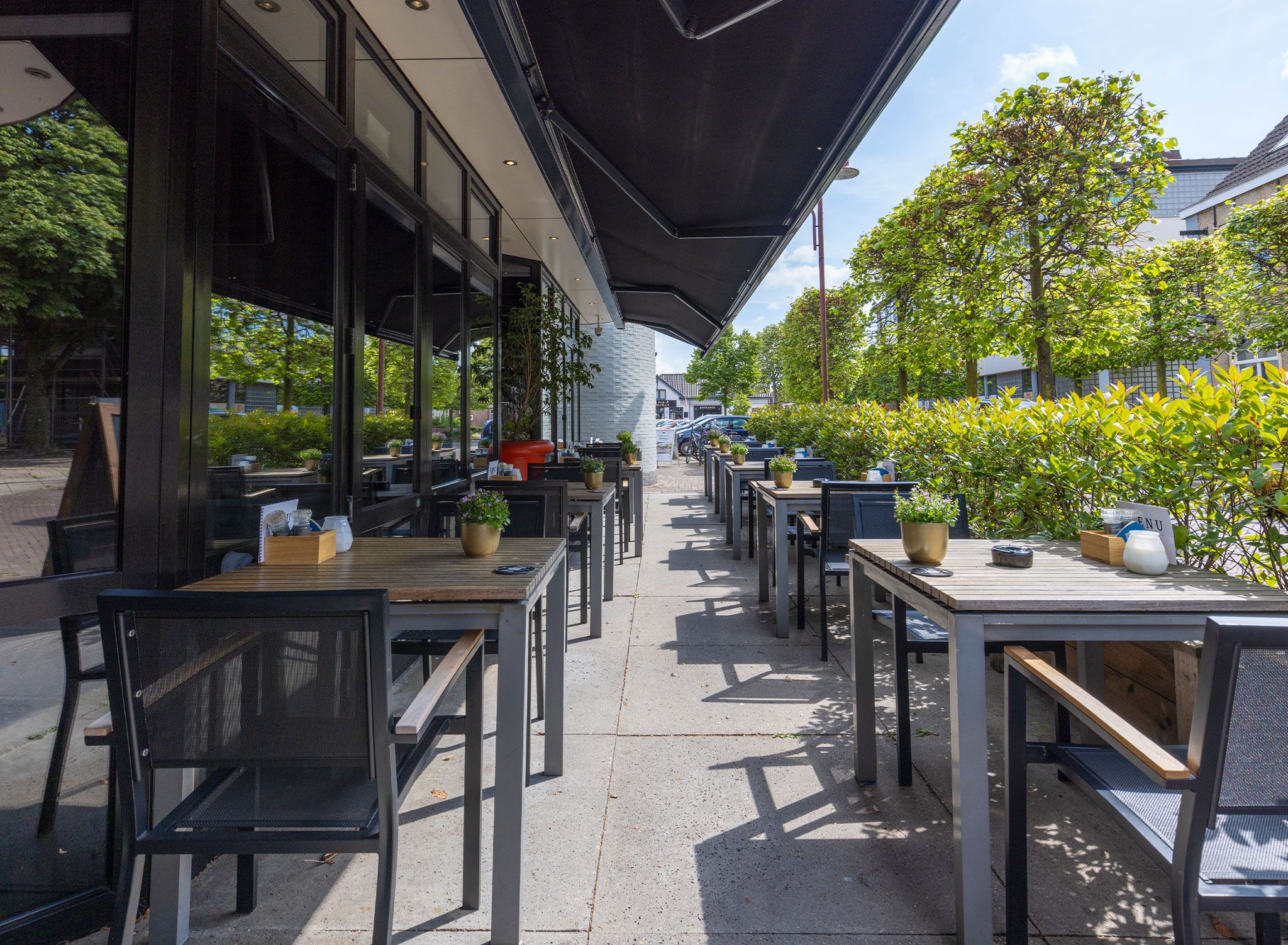 Een terras met tafels, stoelen, een overdekt zitgedeelte en potplanten.