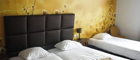 A hotel room with two beds, a dark headboard, and a wall with a floral pattern.