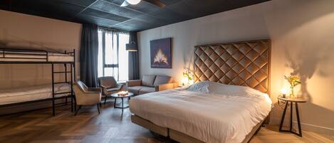 A hotel room with a large bed, a sofa, a chair, a small table, and a ceiling fan.