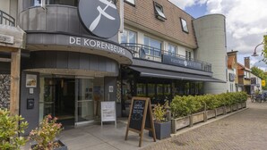 Un bâtiment avec une enseigne indiquant « DE KORENEBURS » et un balcon orné d’une enseigne « FLEISCHER HOTELS ».