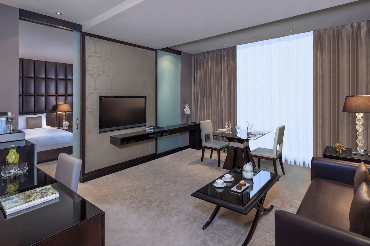 A modern hotel room with a bed, a TV, a dining area, and a sofa.