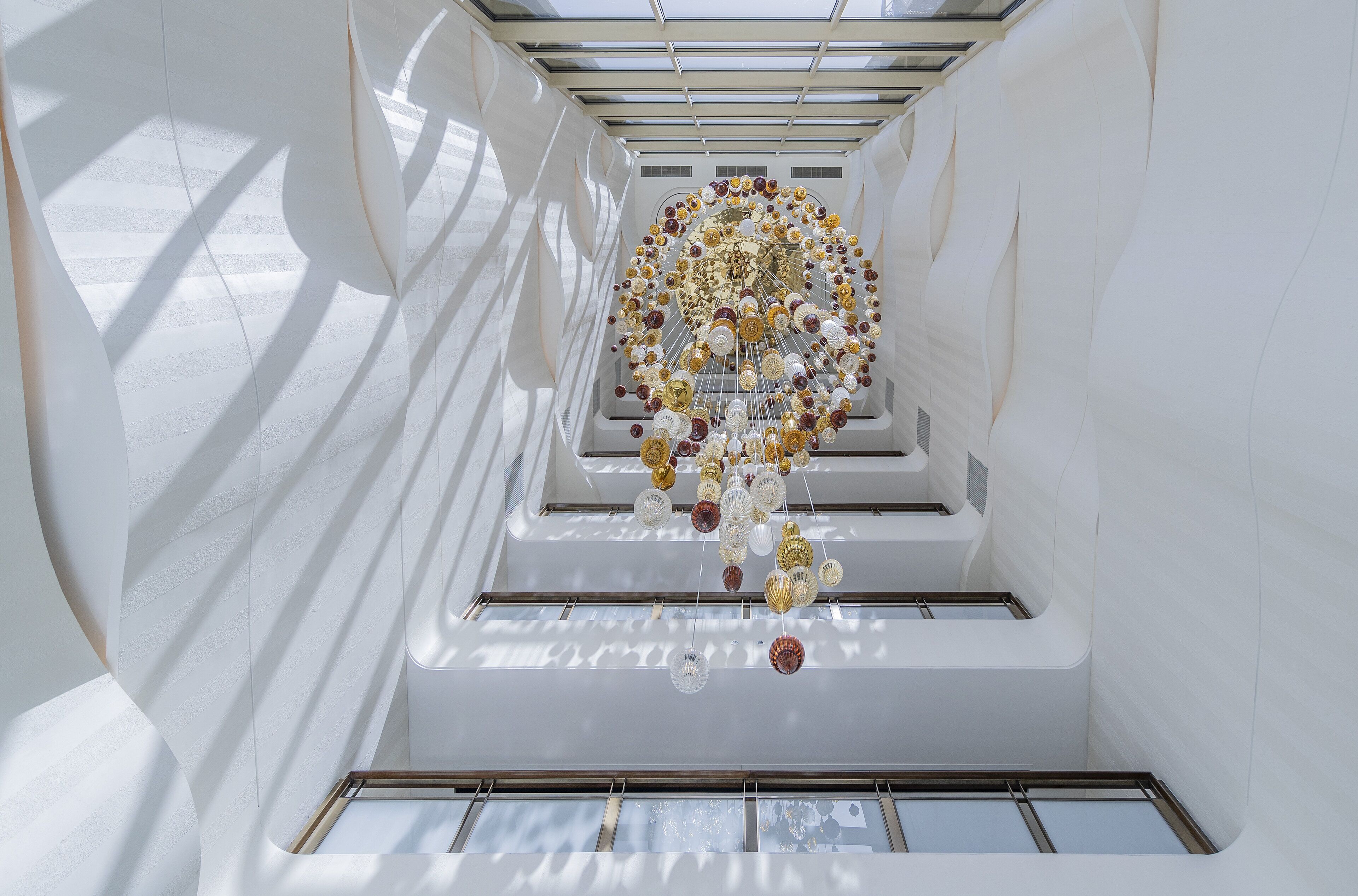 A modern interior with a central spiral staircase, white walls, and a ceiling with a geometric light fixture.