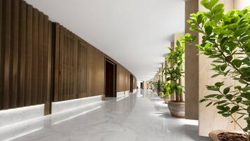 Un pasillo moderno con piso de mármol, paneles de madera en una pared y plantas en macetas en la otra.