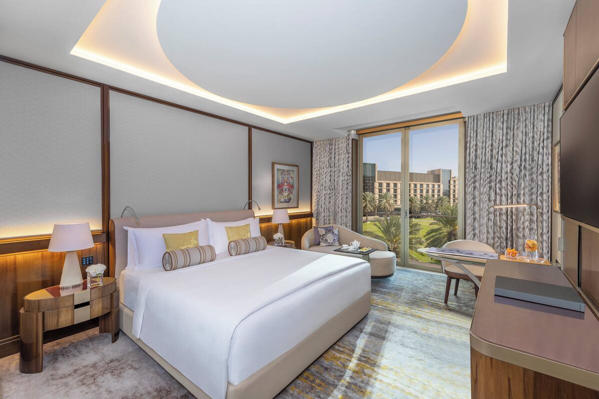 A modern hotel room with a large bed, a desk, and a view of the cityscape.