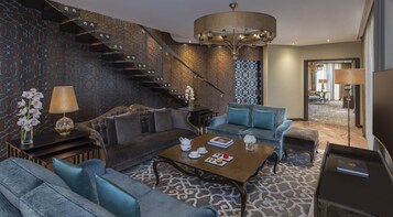 A modern living room with a sofa, armchairs, a coffee table, and a staircase with a patterned wall.