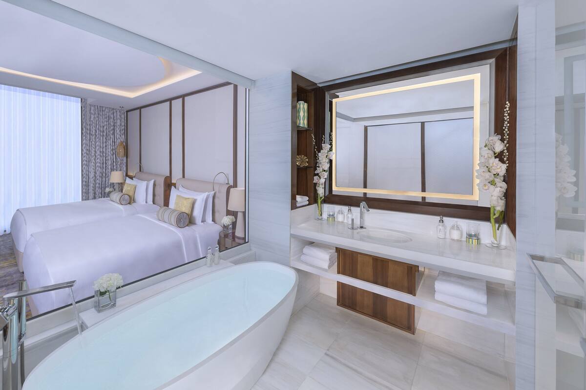 A modern hotel bathroom with a large bathtub, a double sink vanity, and a large mirror.