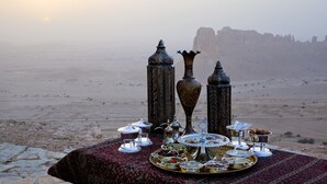 A desert landscape with a table set for a meal featuring traditional Middle Eastern dishes, silverware, and ornate metalware. - Mandarin Oriental Al Faisaliah, Riyadh (Riyadh)