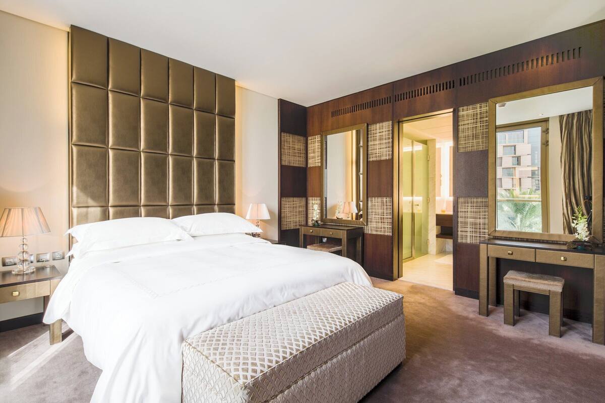 A hotel room with a large bed, a vanity with a mirror, and a view of the outside.