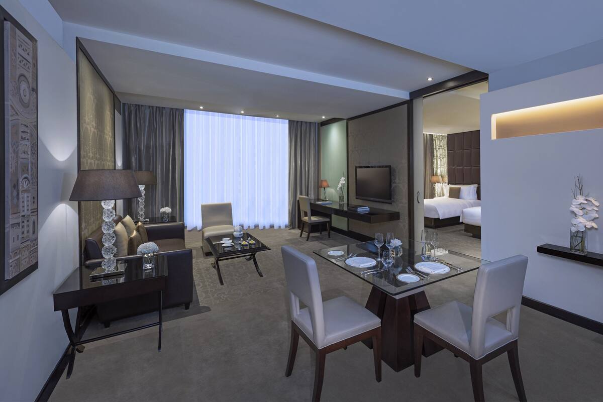 A hotel room with a dining area, a TV, a bed, and a bathroom visible through an open door.