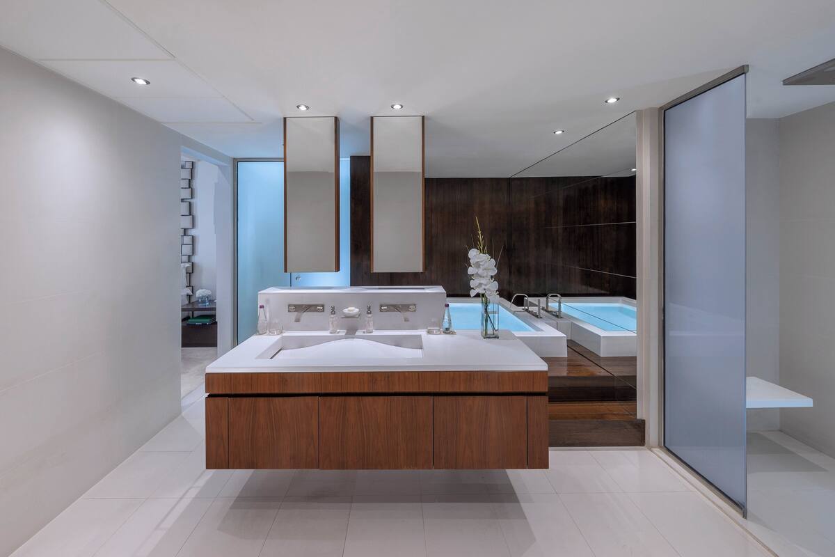 A modern bathroom with a wooden vanity, a large mirror, and a bathtub.