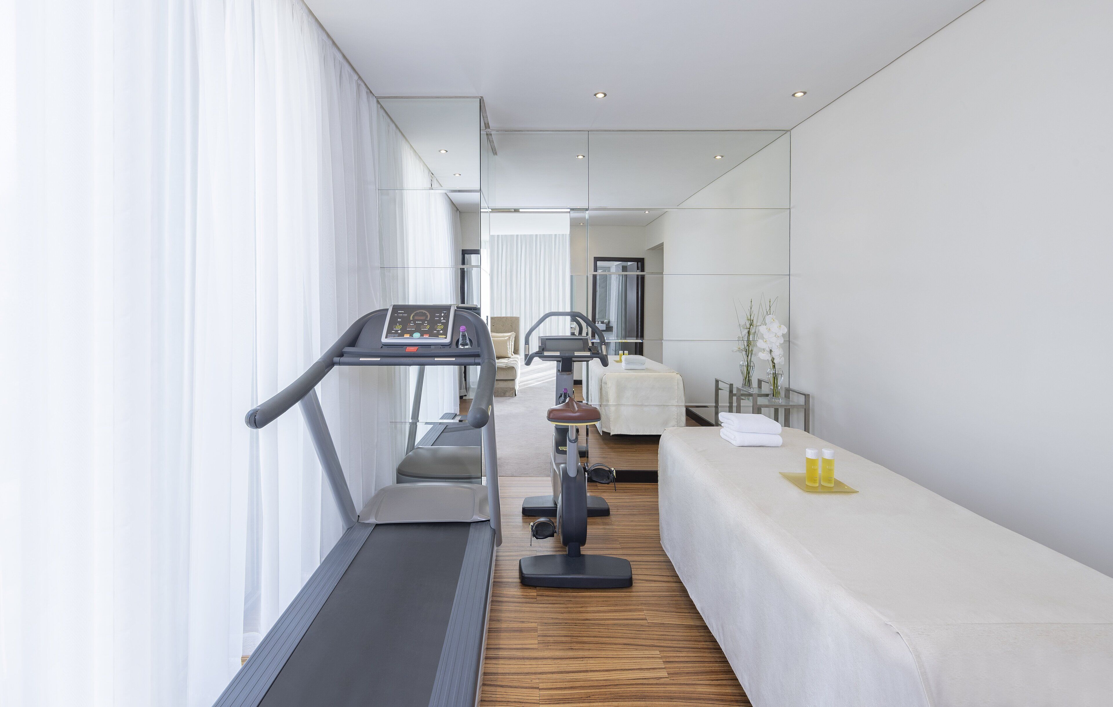 A modern hotel room with a treadmill, exercise bike, and a massage table.