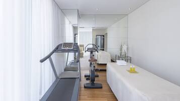 A modern hotel room with a treadmill, exercise bike, and a massage table.