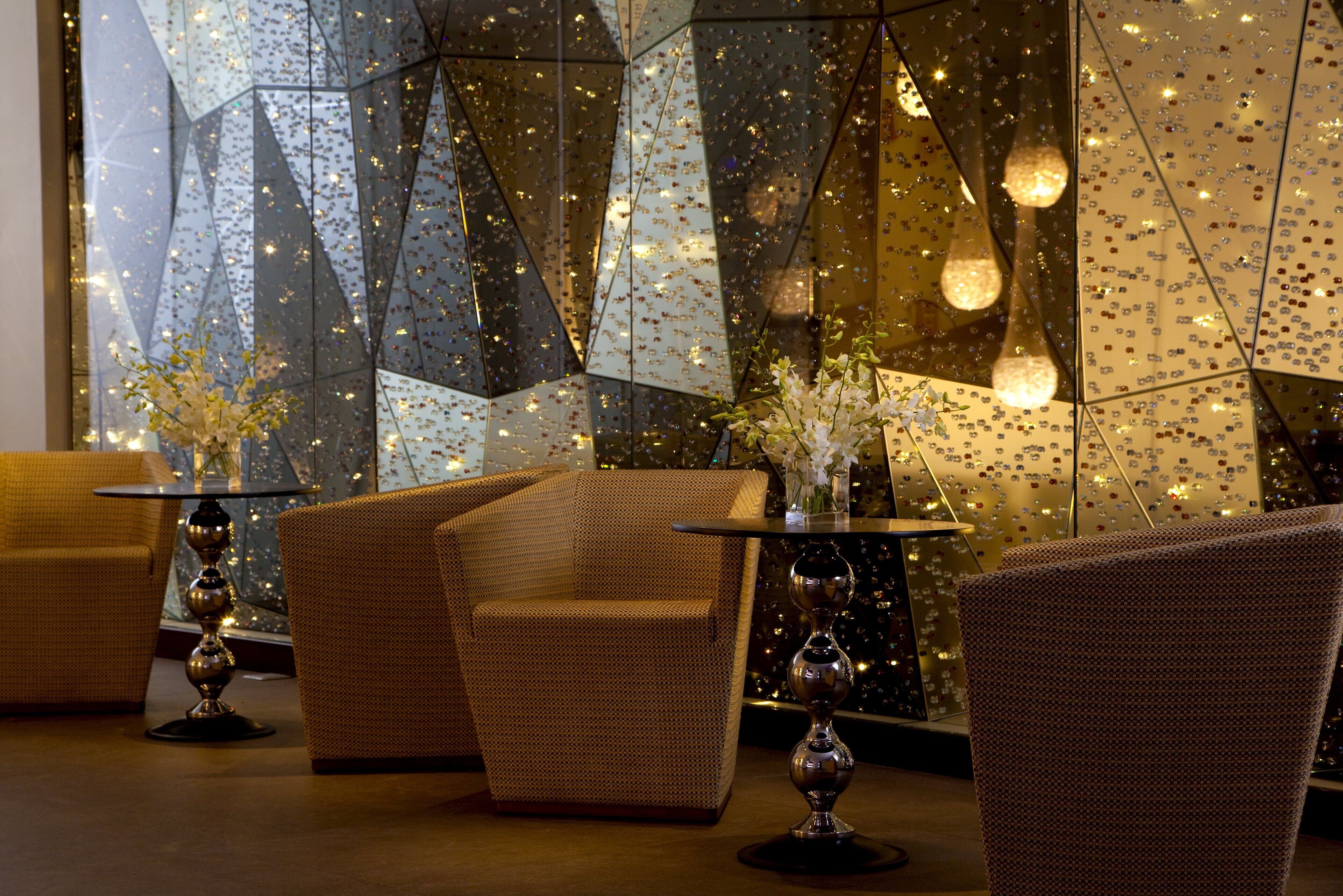 Un interior moderno con patrones geométricos en la pared, dos sofás, una mesa con un florero y luces decorativas.