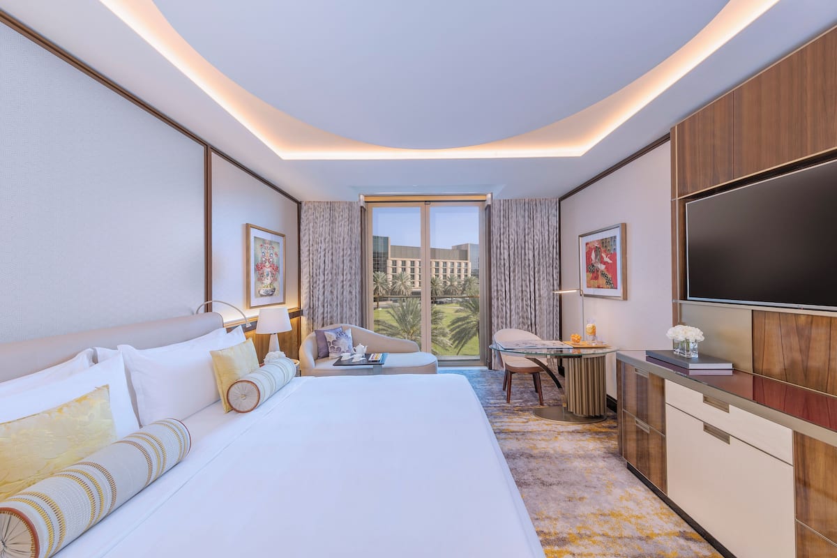 A modern hotel room with a large bed, a desk, a TV, and a view of the city.