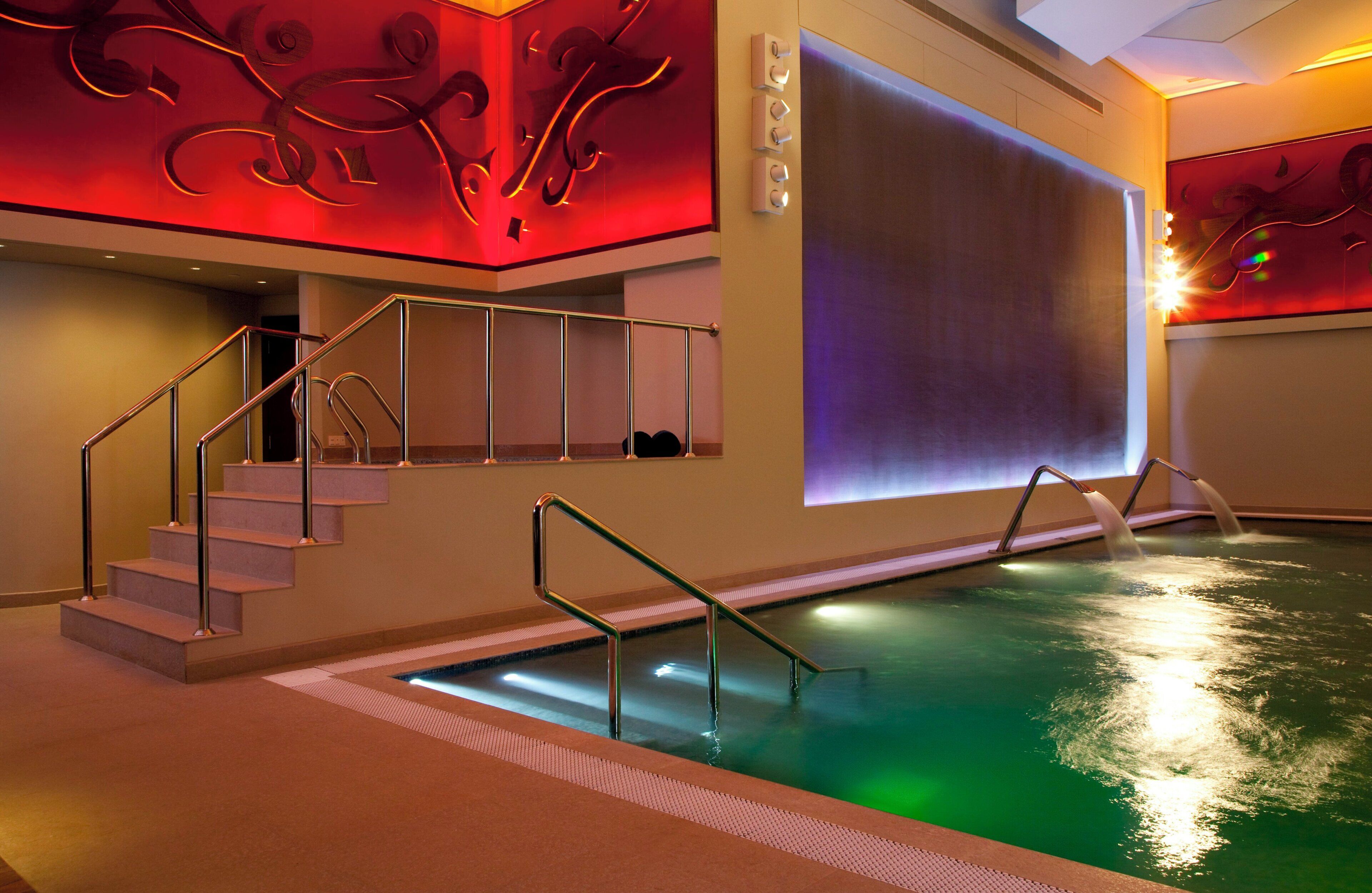 A hotel room with a pool, a staircase, and a large screen.