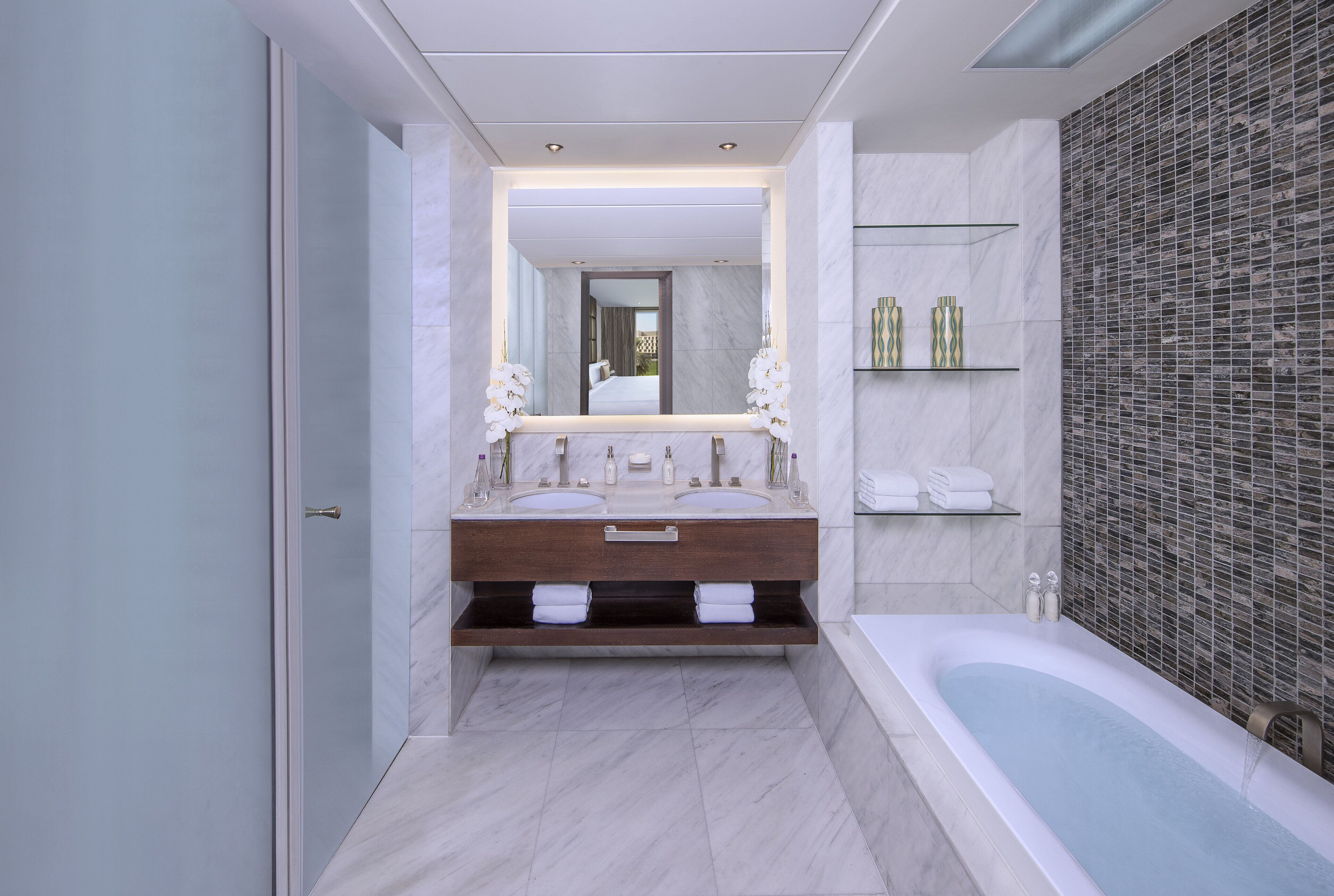 A modern bathroom with a large mirror, a double sink vanity, a bathtub, and a shower area.