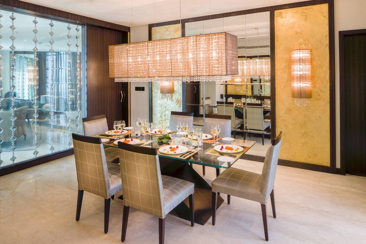 A dining area with a glass table, cushioned chairs, and a chandelier.