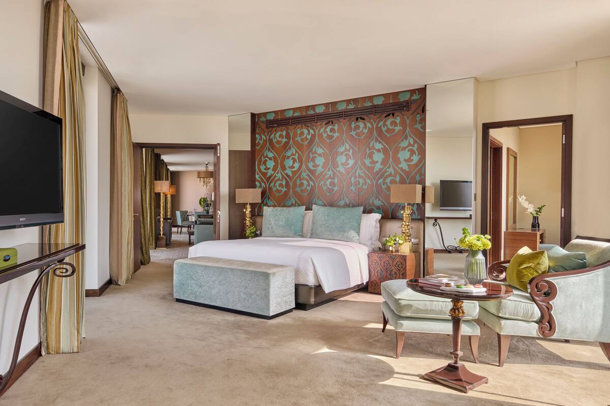 A hotel room with a large bed, a TV, a desk with a lamp, and a sofa.