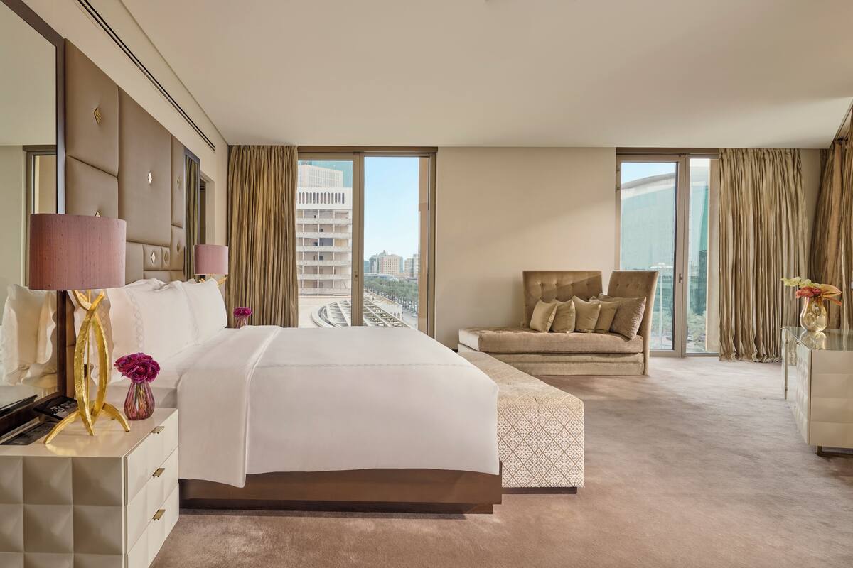 A hotel room with a large bed, a sofa, a TV, and a view of the city.