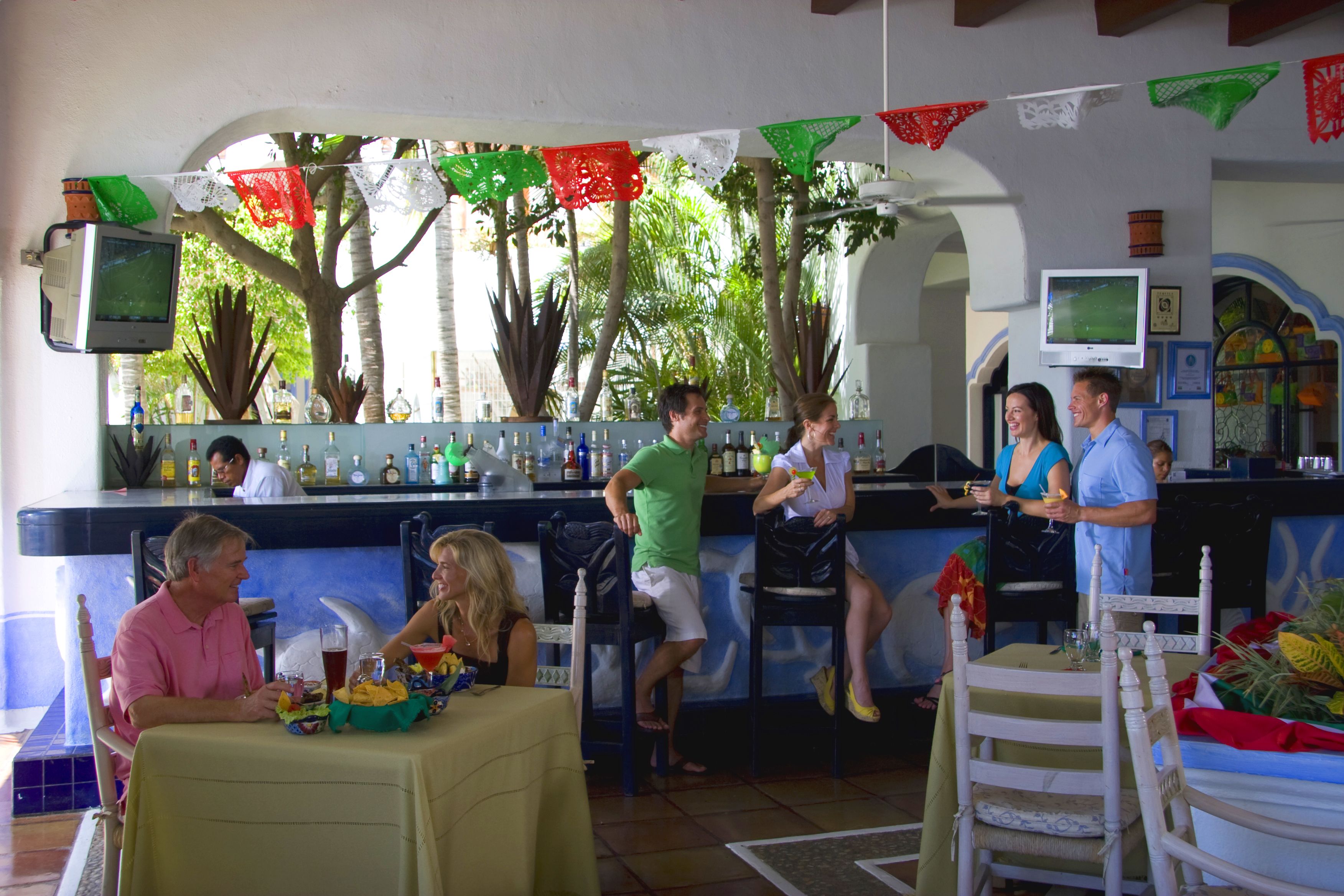 A bar area with a counter, chairs, and tables. There are decorative flags hanging above the bar.