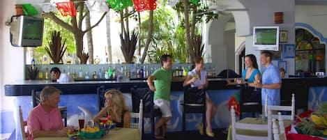 A bar area with a counter, chairs, and tables. There are decorative flags hanging above the bar.