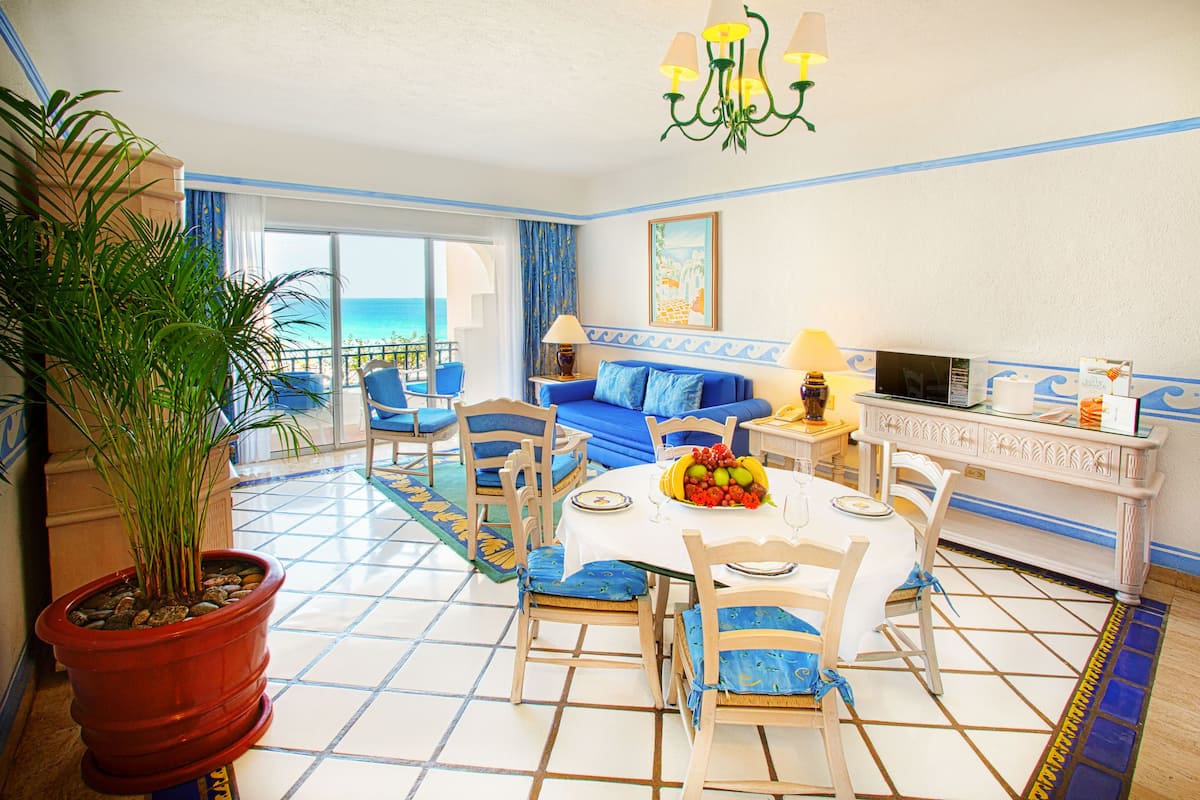 A dining area with a table set for four, blue upholstered chairs, a potted plant, and a view of the ocean through large windows.
