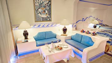 Une chambre d’hôtel avec un canapé bleu, une table à manger recouverte d’une nappe blanche et un lit agrémenté d’une couvre-lit à motifs.