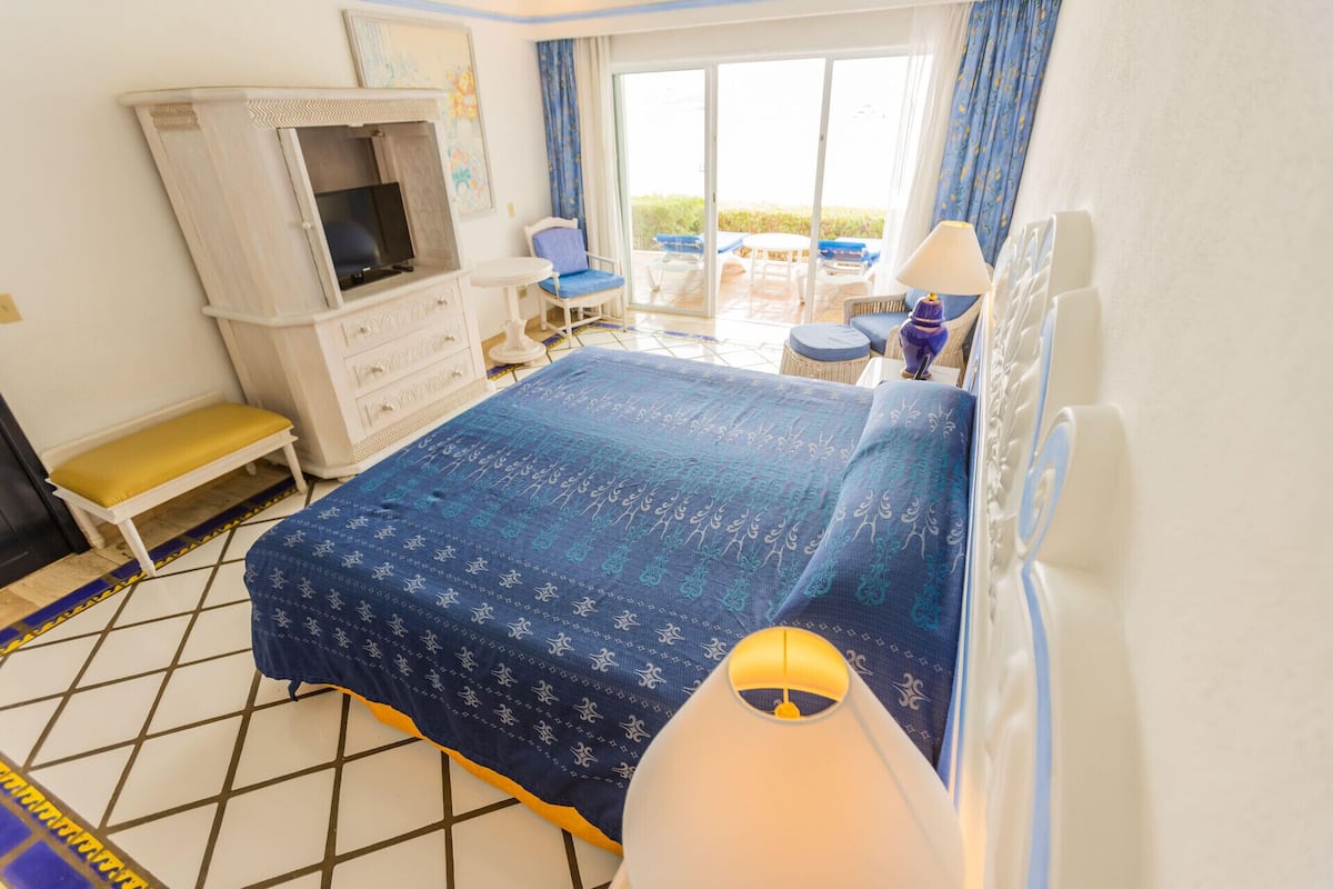 A hotel room with a bed, a TV, a chair, a table, and a view of the outdoors.