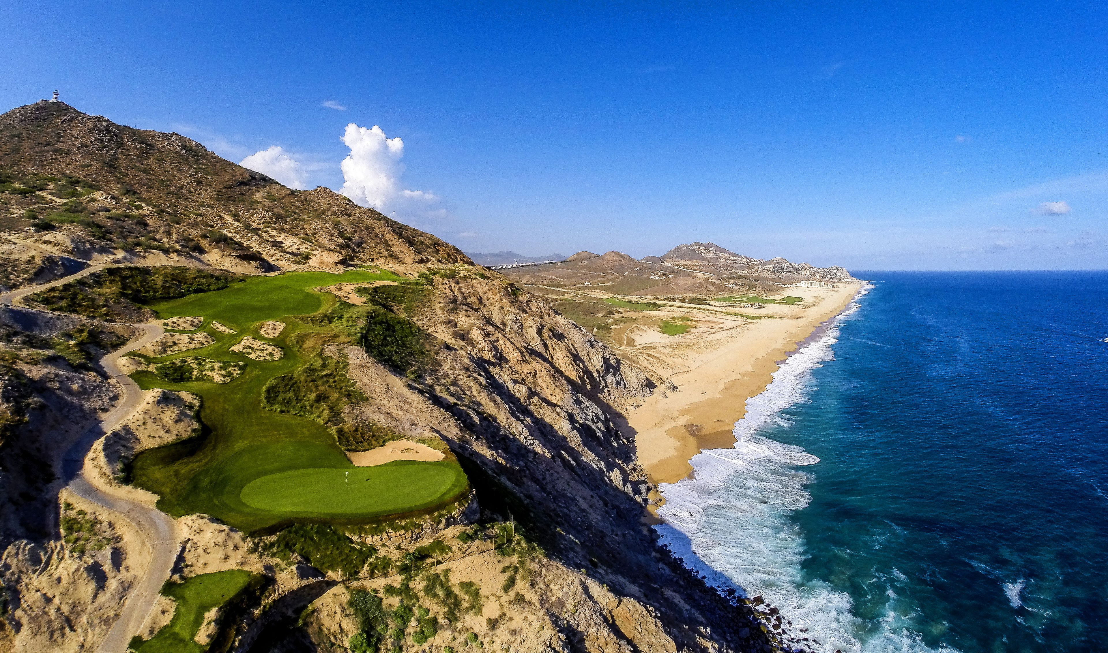 A coastal landscape with a golf course, a beach, and a rocky cliff.