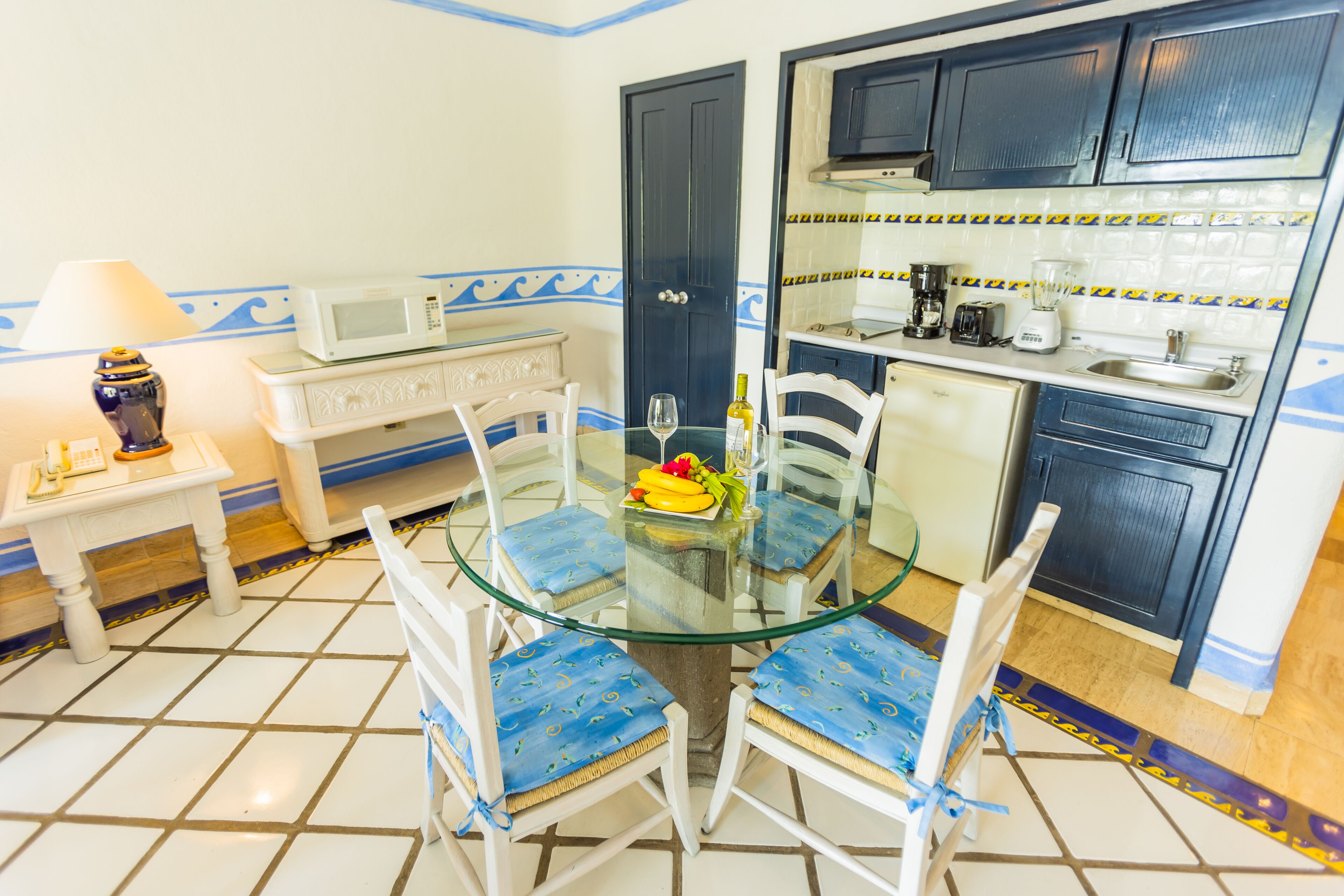 Una cocina compacta con una mesa de comedor de vidrio rodeada de sillas blancas, un microondas y una cafetera.