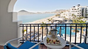 Un balcone con un tavolo apparecchiato per un pasto, con vista su una spiaggia e una zona piscina.