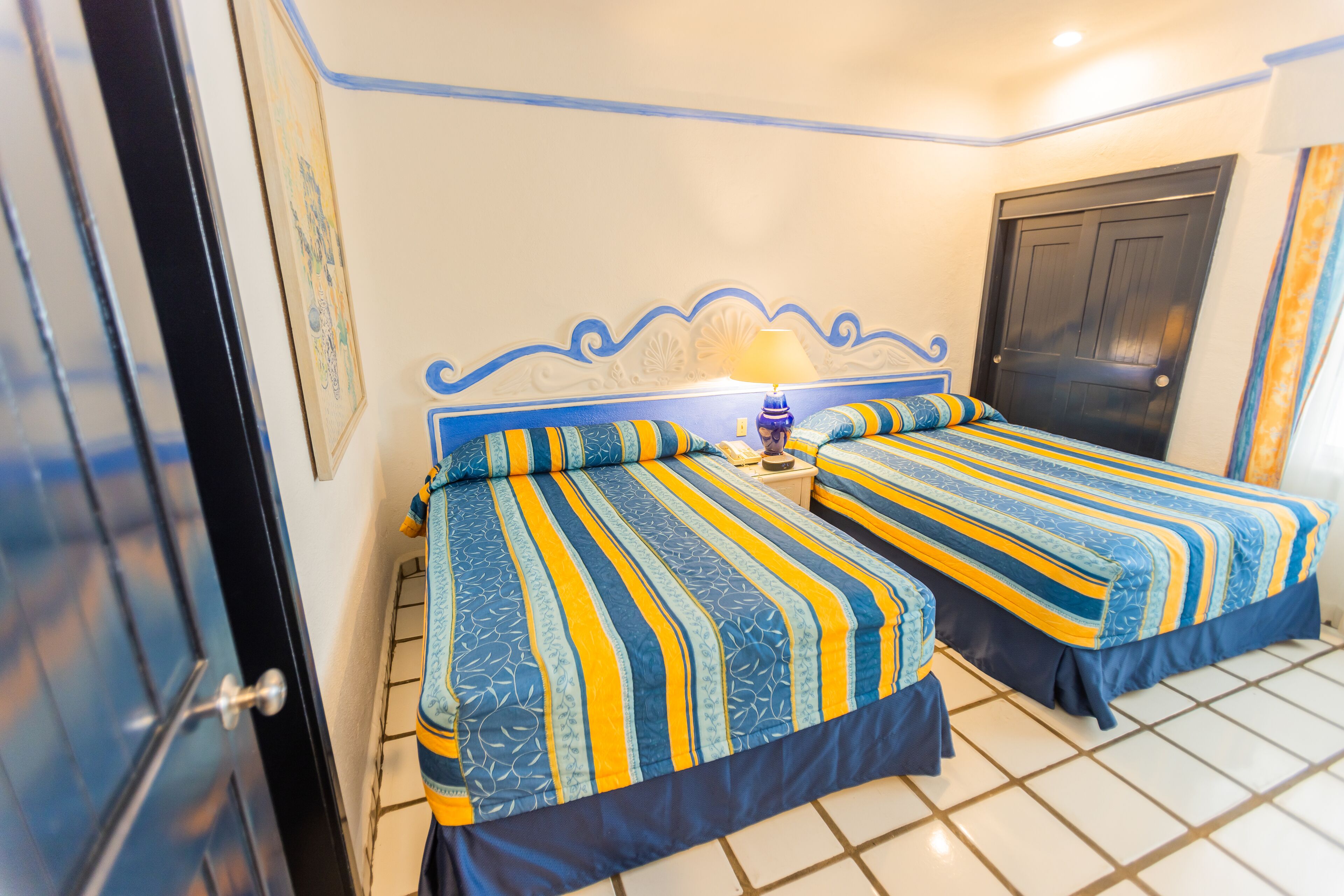 A room with two beds, each with striped bedding, a nightstand with a lamp, and a door.
