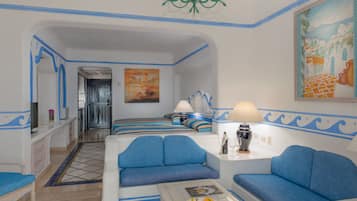 Une chambre d’hôtel moderne aux couleurs bleu et blanc, comprenant un canapé, une petite table avec une assiette de fruits et un tableau accroché au mur.